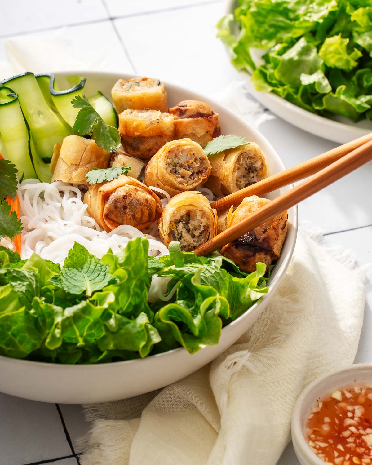 Lifting up sliced vietnamese egg rolls from a bowl of bun cha gio.