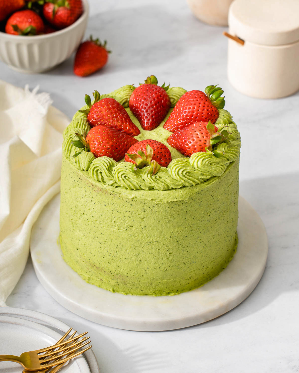 A matcha cake with strawberries served on a marble tray.
