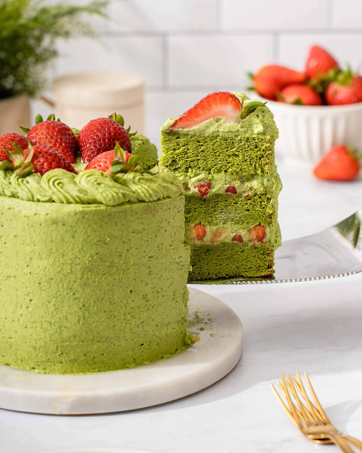 Someone lifting out a slice of matcha cake from a whole cake.