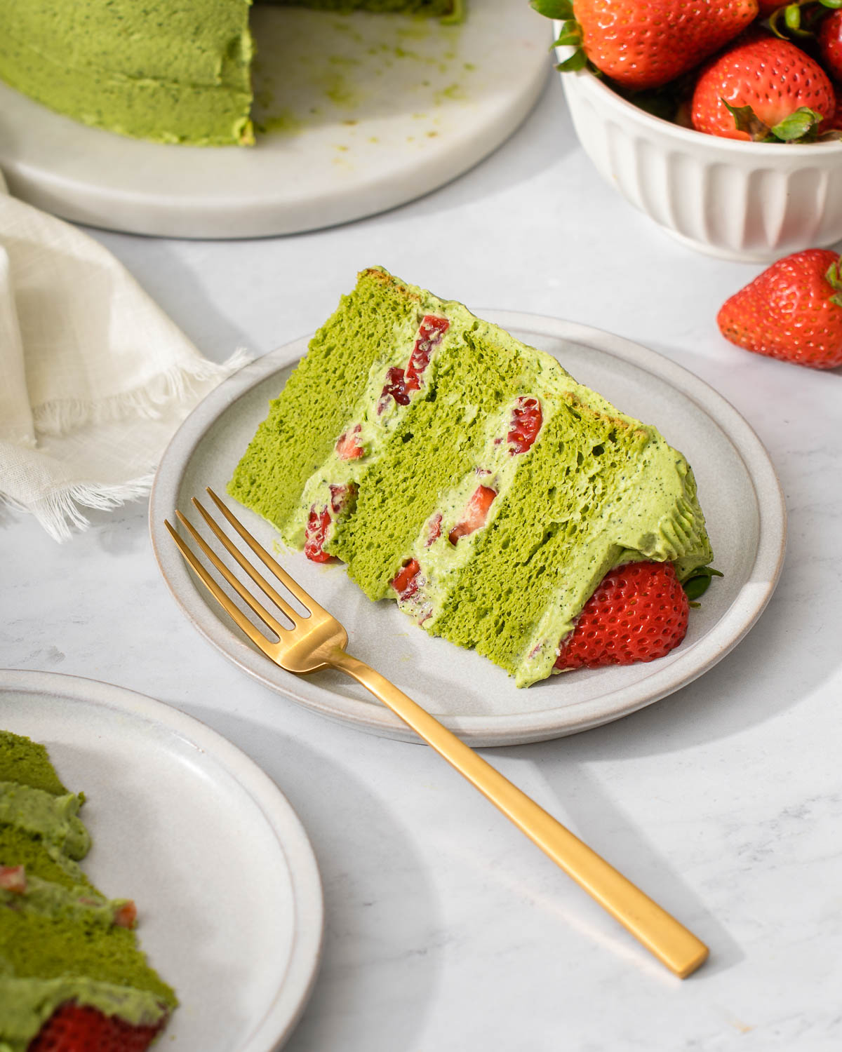 A slice of matcha cake with strawberries resting on a dessert plate.