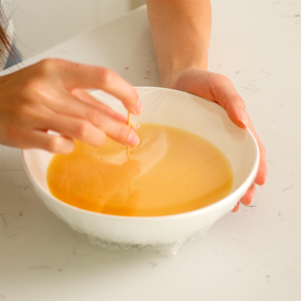 Poking holes into a plastic wrapped bowl with egg mixture inside.