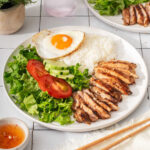 A plate of vietnamese lemongrass chicken with all the sides on a tile table.
