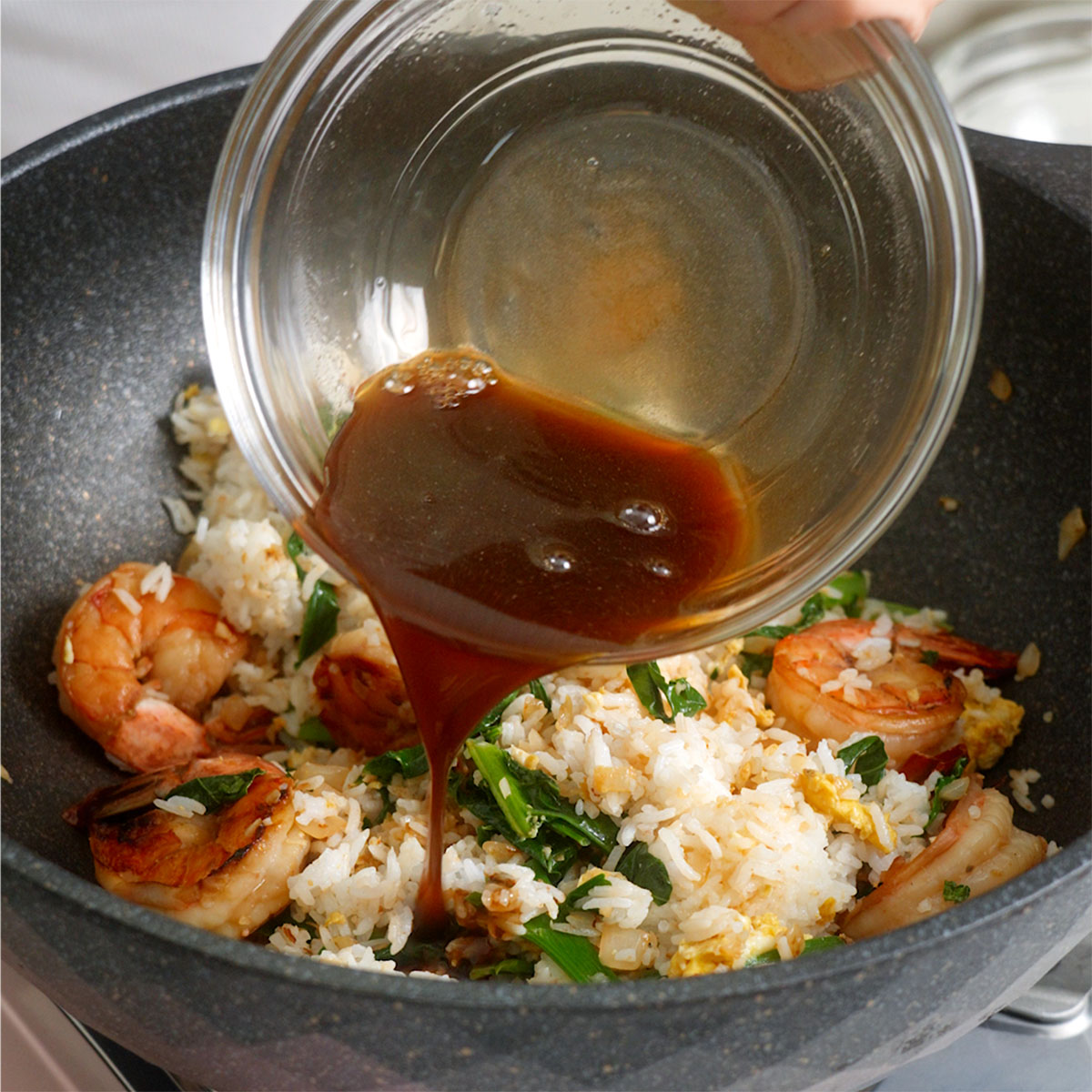 Pouring Thai Fried Rice sauce into a wok with fried rice.