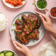 Someone placing a plate of bulgogi chicken onto a tiled table.