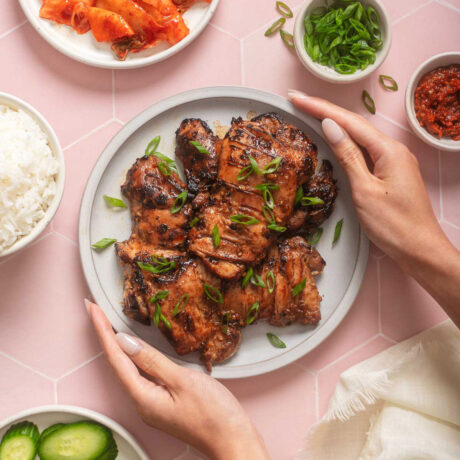 Someone placing a plate of bulgogi chicken on to a tiled table.