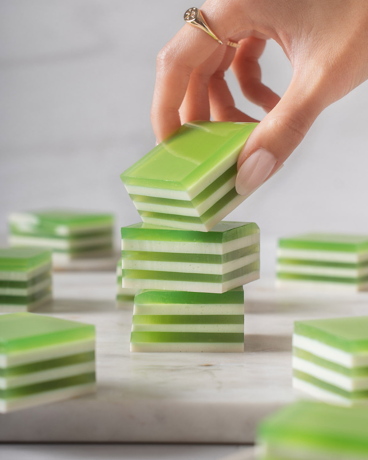 Someone lifting up a square of coconut pandan jelly from a stack of jellies.
