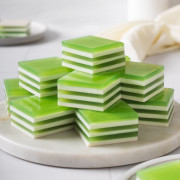 A round tray stacked with layered coconut pandan jelly.