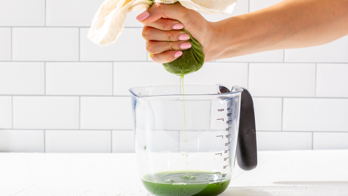 Squeezing pureed pandan leaves to juice into a measuring cup.