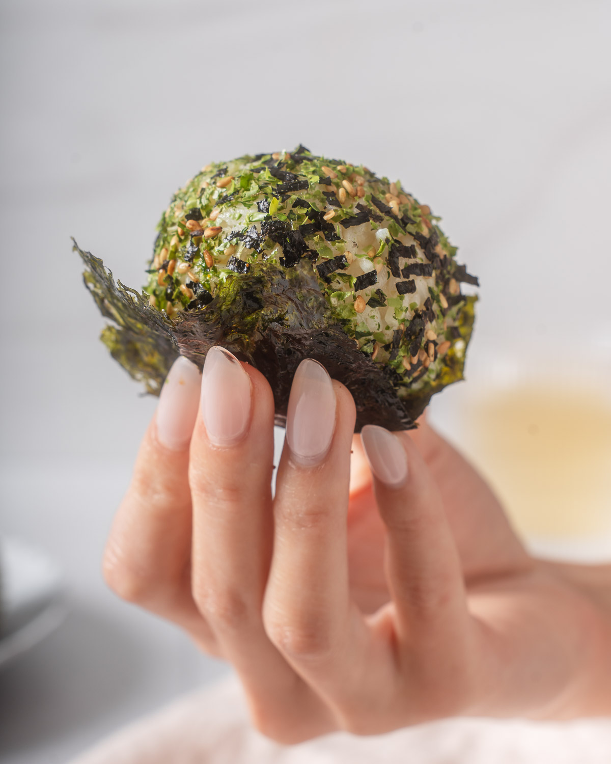 Someone holding up a korean rice ball with a seaweed snack.