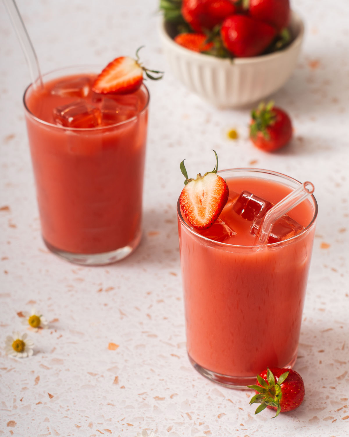 Two glasses of strawberry green tea with a bowl of strawberries nearby.