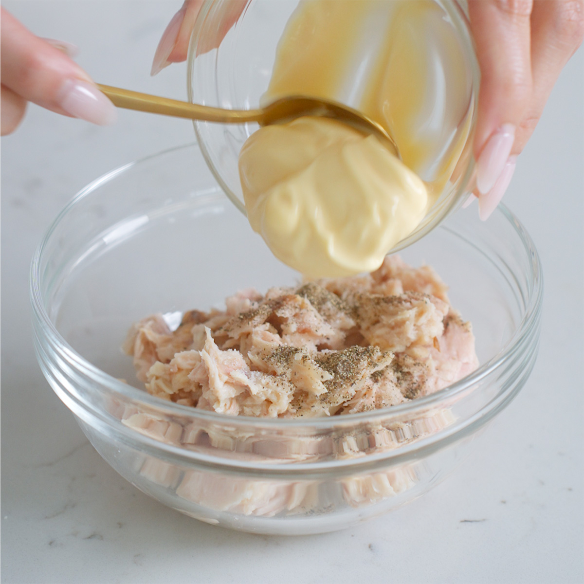 Adding kewpie mayo to a bowl with canned tuna.