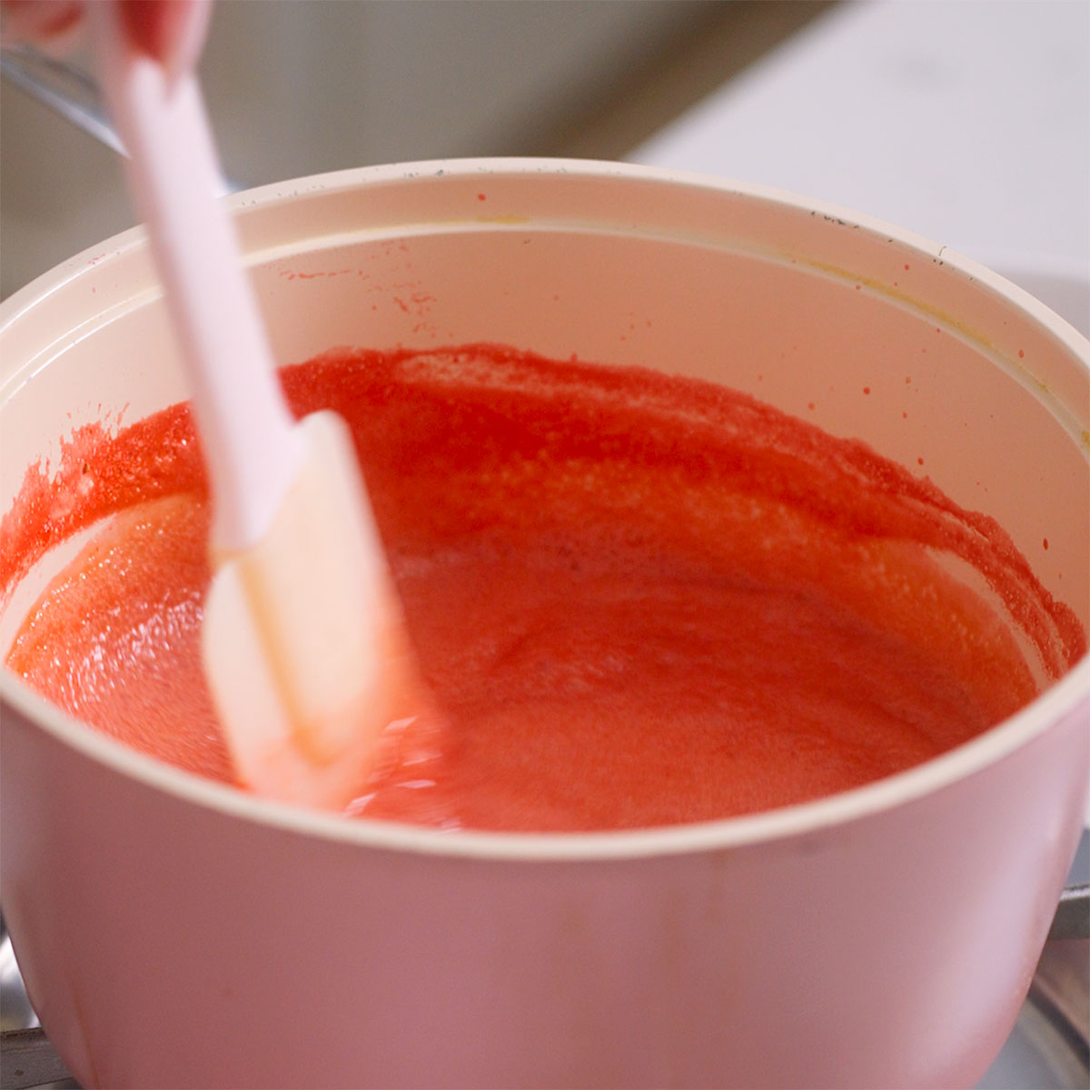 Stirring strawberry puree that is simmering on the stove.