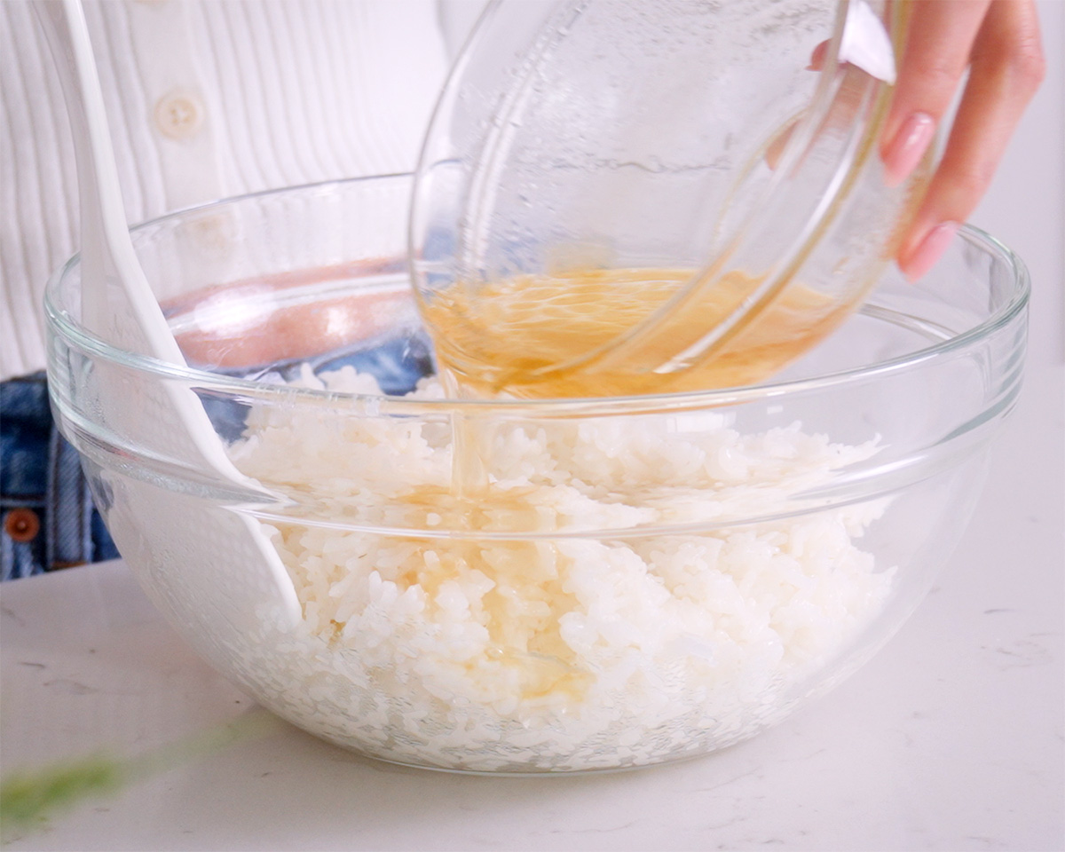 Pouring the seasoning into a bowl of cook sushi rice.