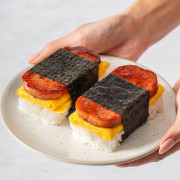 Someone holding a plate with two spam musubis with egg.
