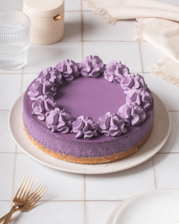 An ube cheesecake on a serving plater with forks nearby.