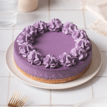 An ube cheesecake on a serving plater with forks nearby.