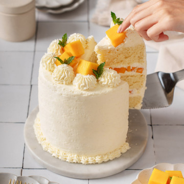Someone lifting a slice of mango cake from a full cake.