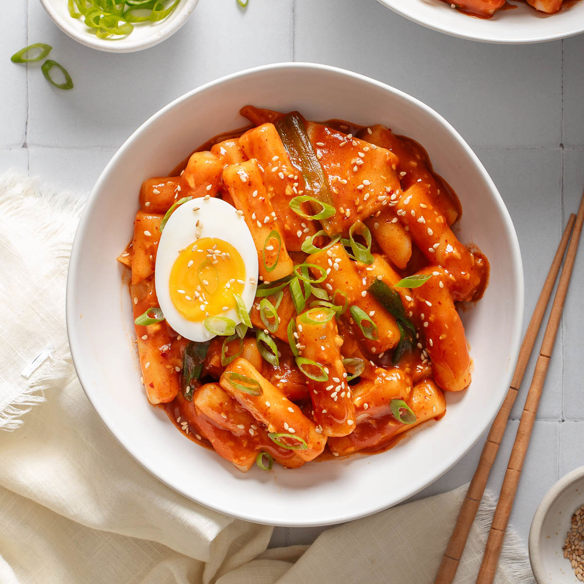 Looking down at a bowl of tteokbokki garnished with sesame seeds and an egg.