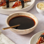 Unagi sauce in a bowl with unagi sushi nearby.