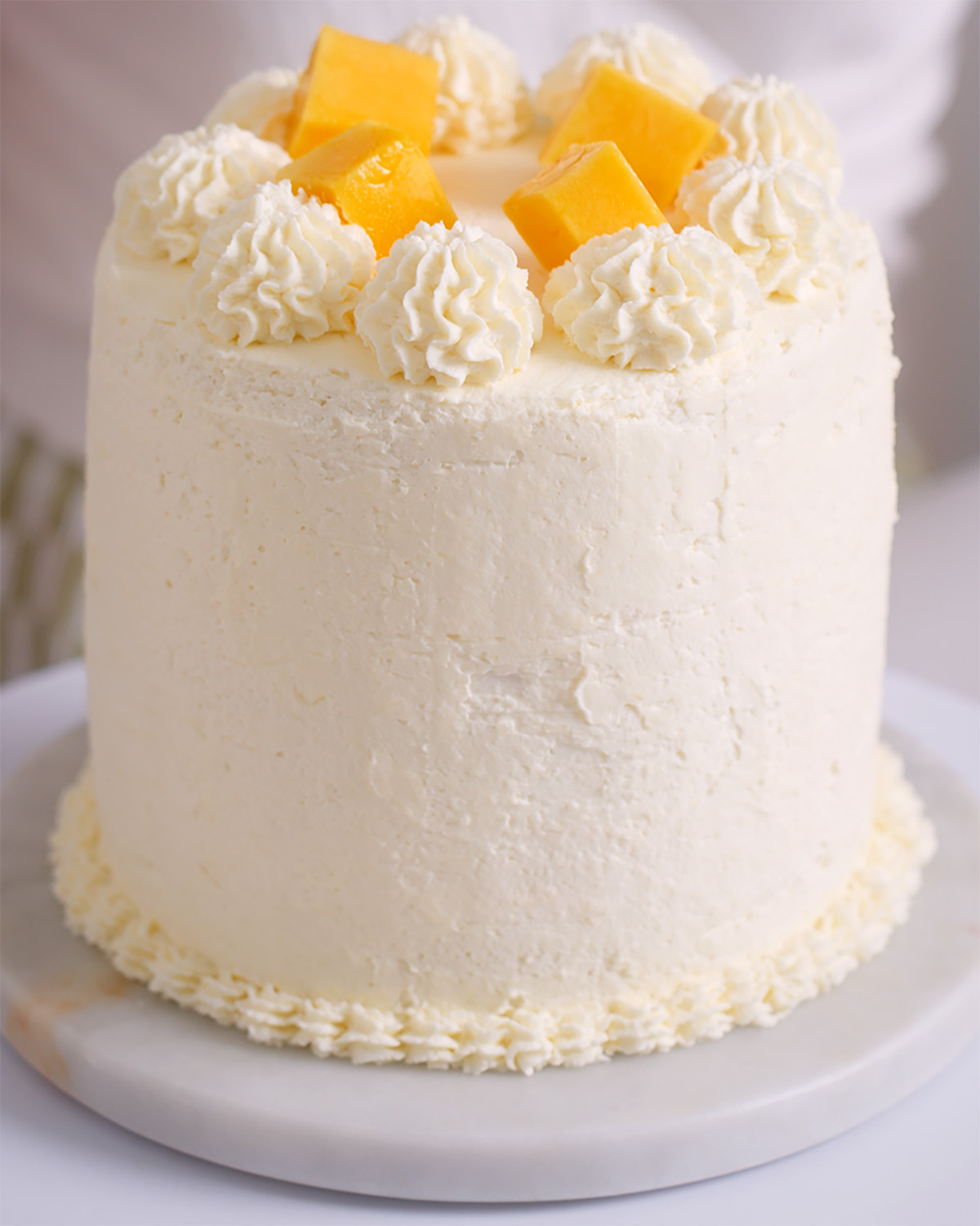 Decorating a mango cake with whipped cream frosting.