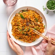 Someone holding a plate of bami goreng and a pair of chopsticks.