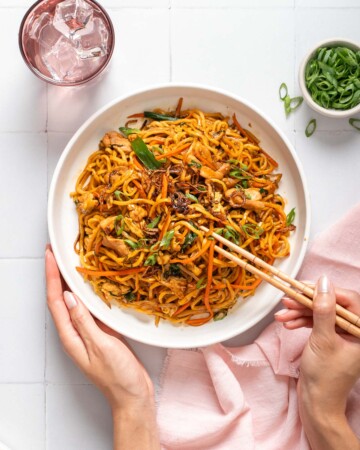 Một người đang cầm một đĩa bami goreng và một đôi đũa.