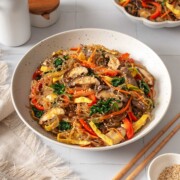 A bowl of japchae surrounded by table settings.