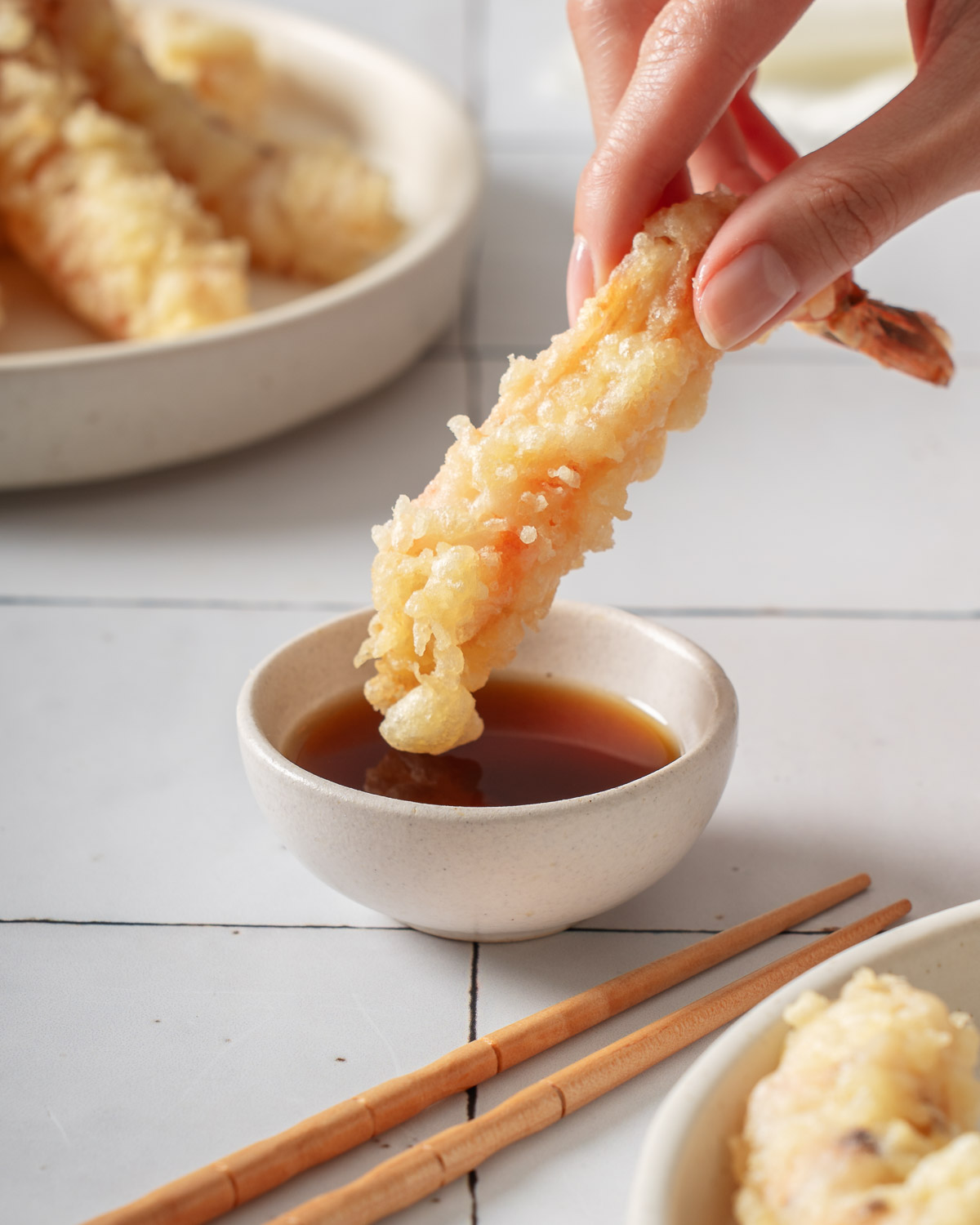 Someone dipping a shrimp tempura into a small ramekin of tempura dipping sauce.