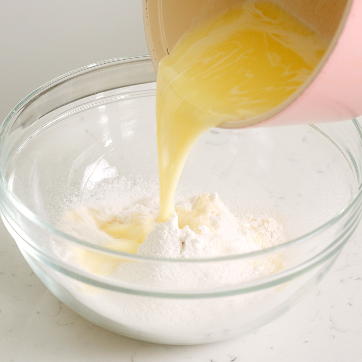 Pouring melted butter and milk into a bowl of sifted flour.