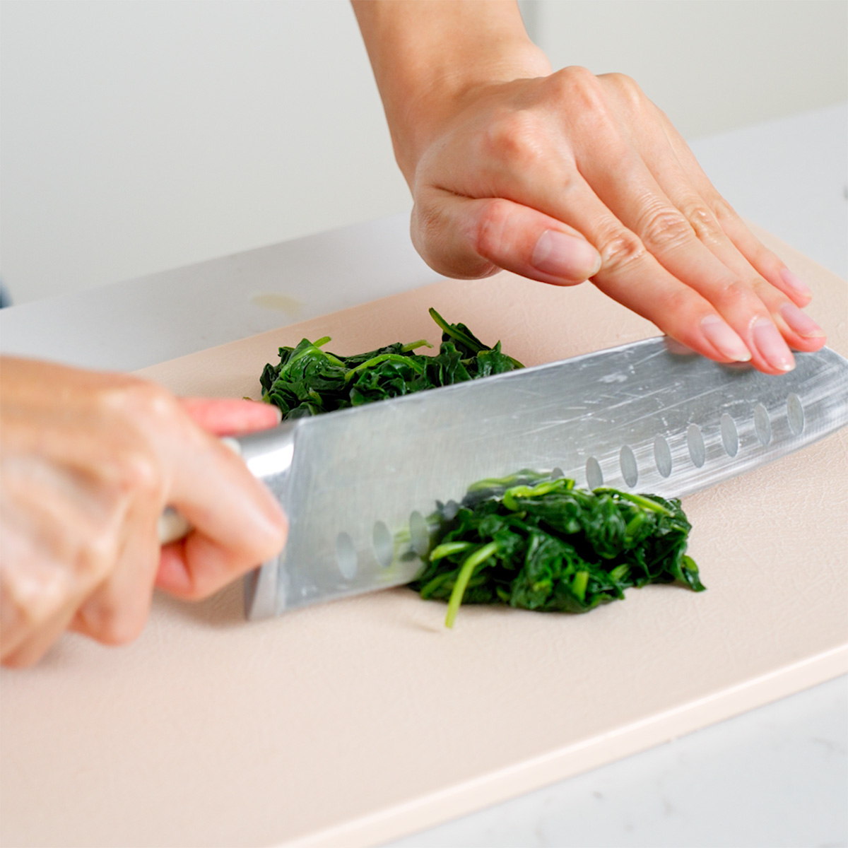 Chopping blanched spinach on a cutting board.