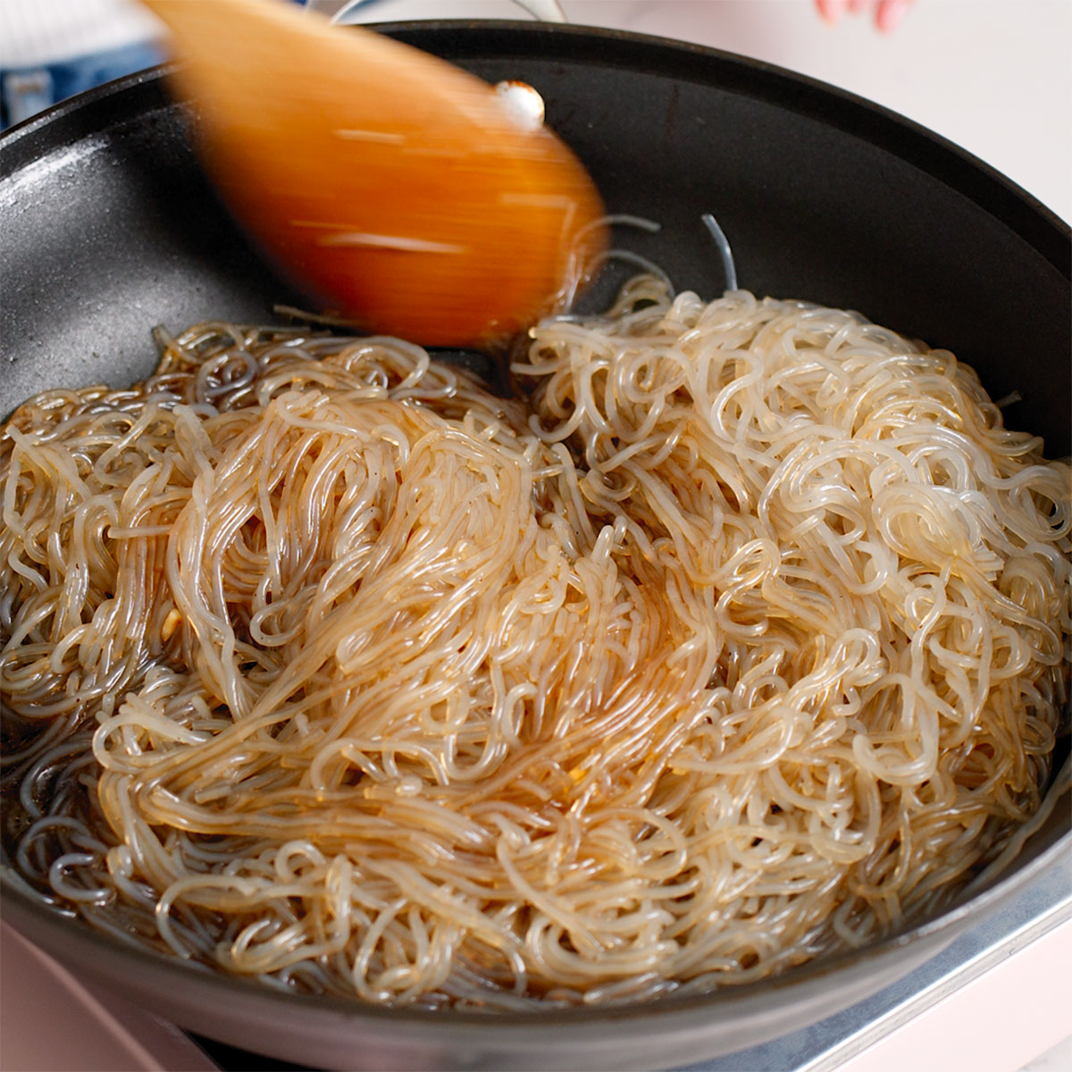 Cooking glass noodles with japchae sauce in a large skillet.