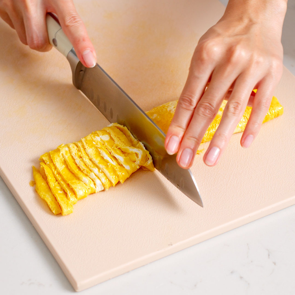 Slicing a rolled egg omelette into thin strips of egg.