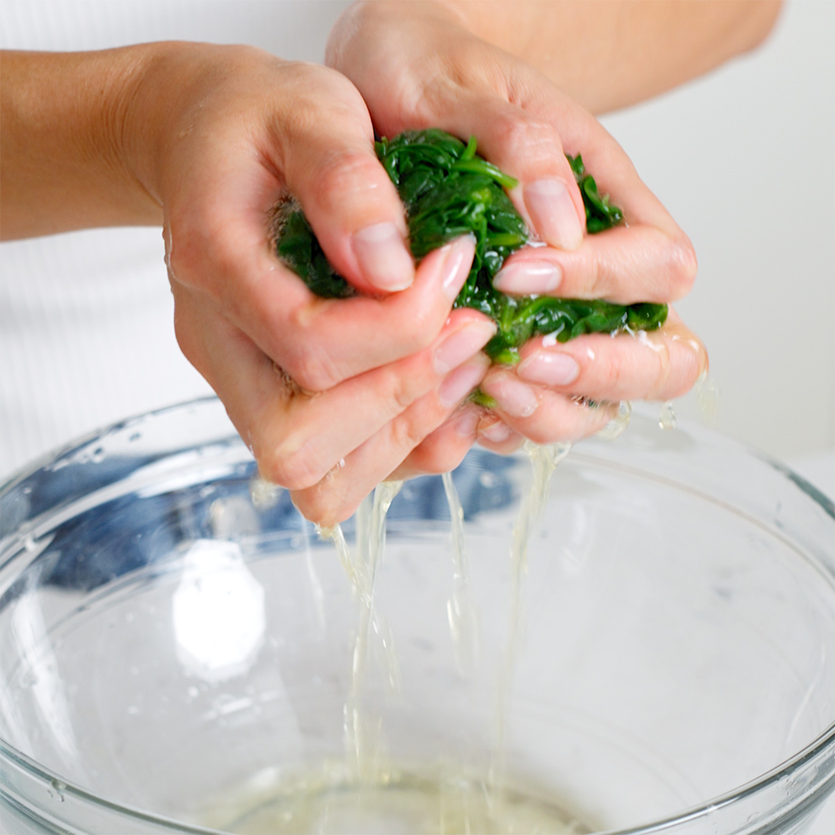 Squeezing out excess water from a ball of blanched spinach.