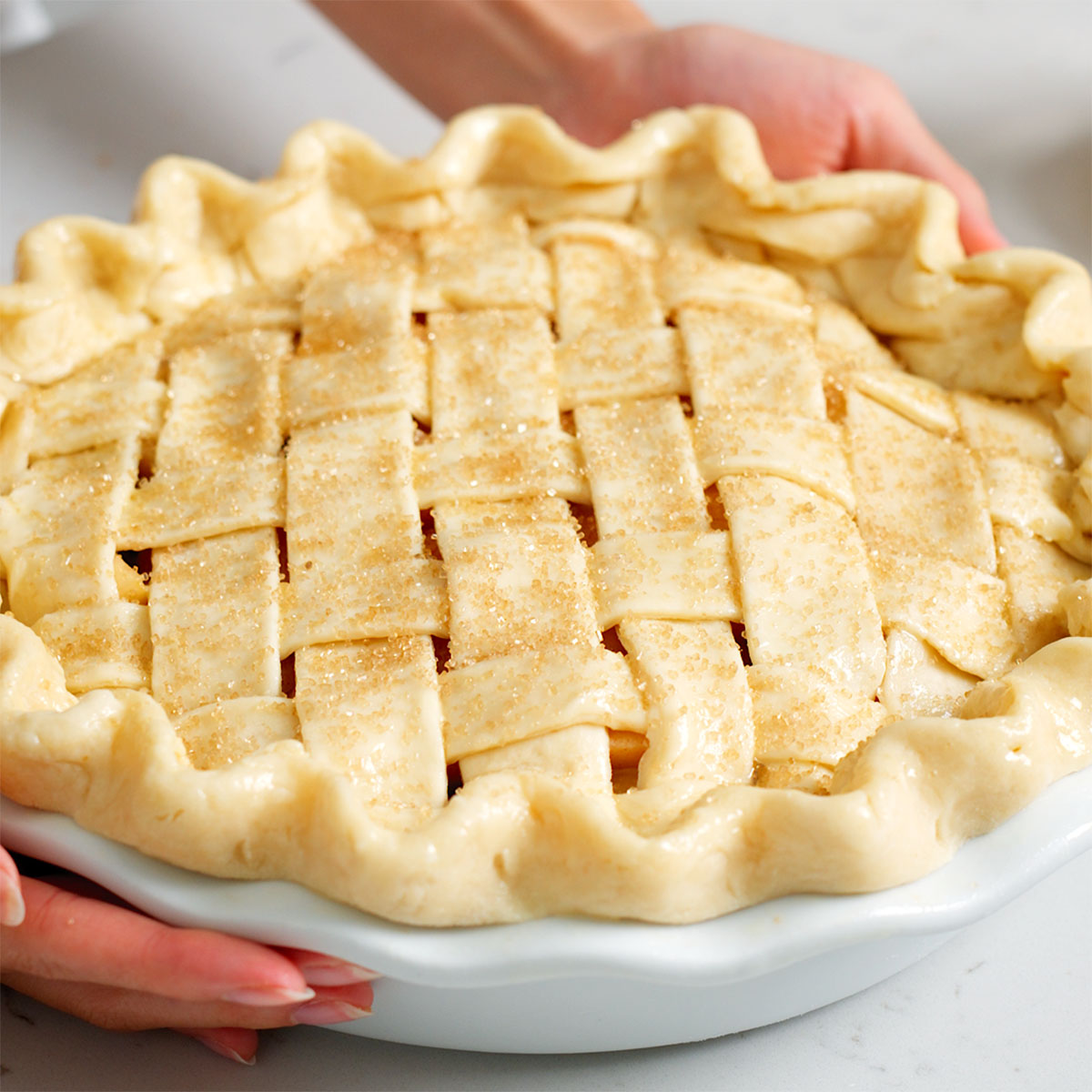 An apple pie topped with coarse sugar ready for baking.