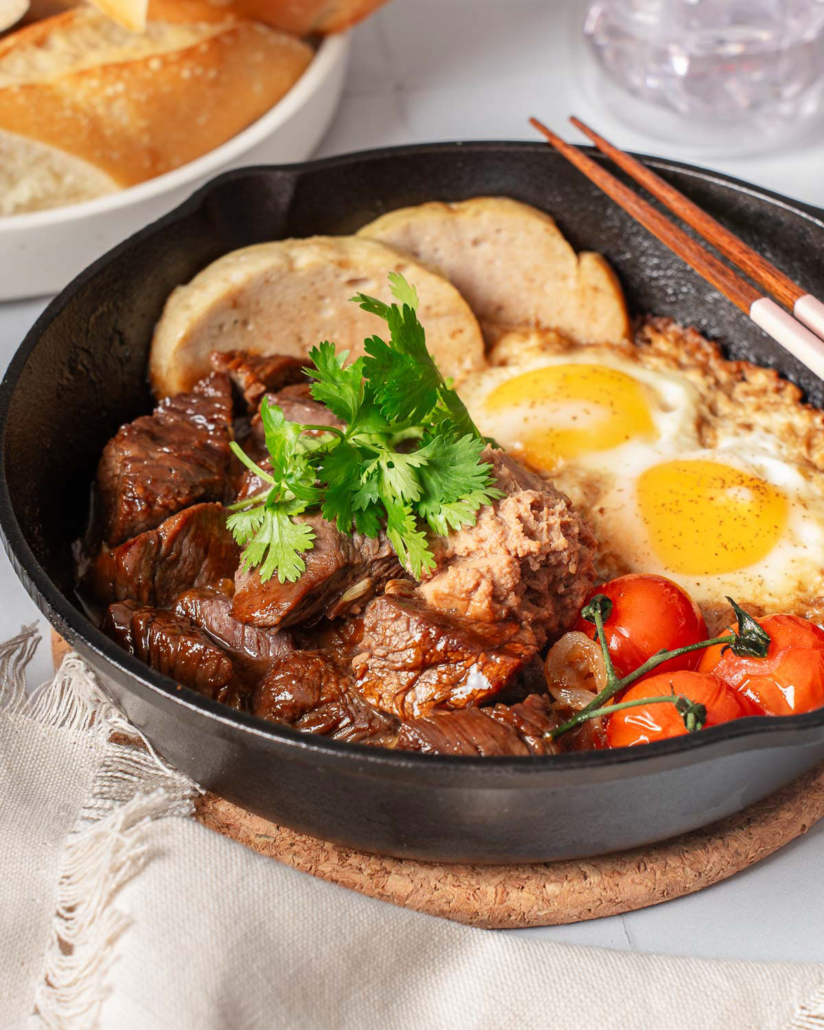 A skillet with Vietnamese style steak and eggs garnished and served with chopsticks.