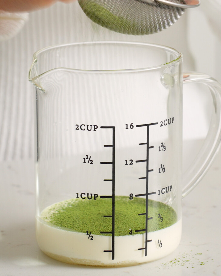 Sifting matcha powder into a measuring cup for matcha foam.