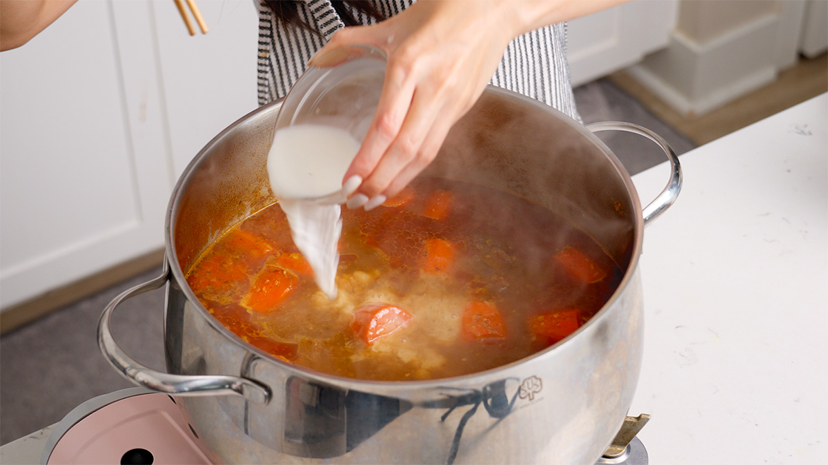 Adding cornstarch slurry to a large pot of Vietnamese beef stew.