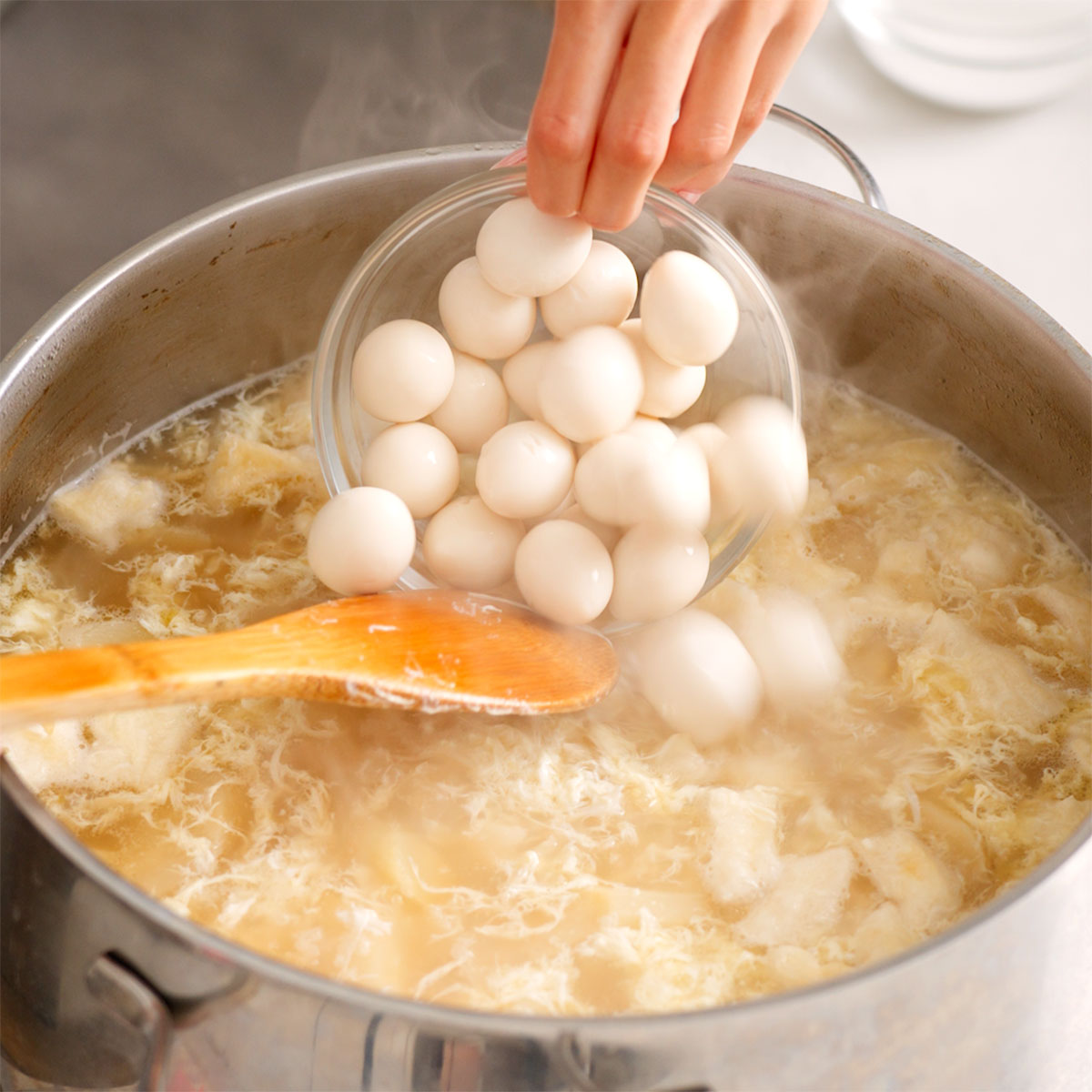 Adding quail eggs to a pot of vietnamese crab and asparagus soup.