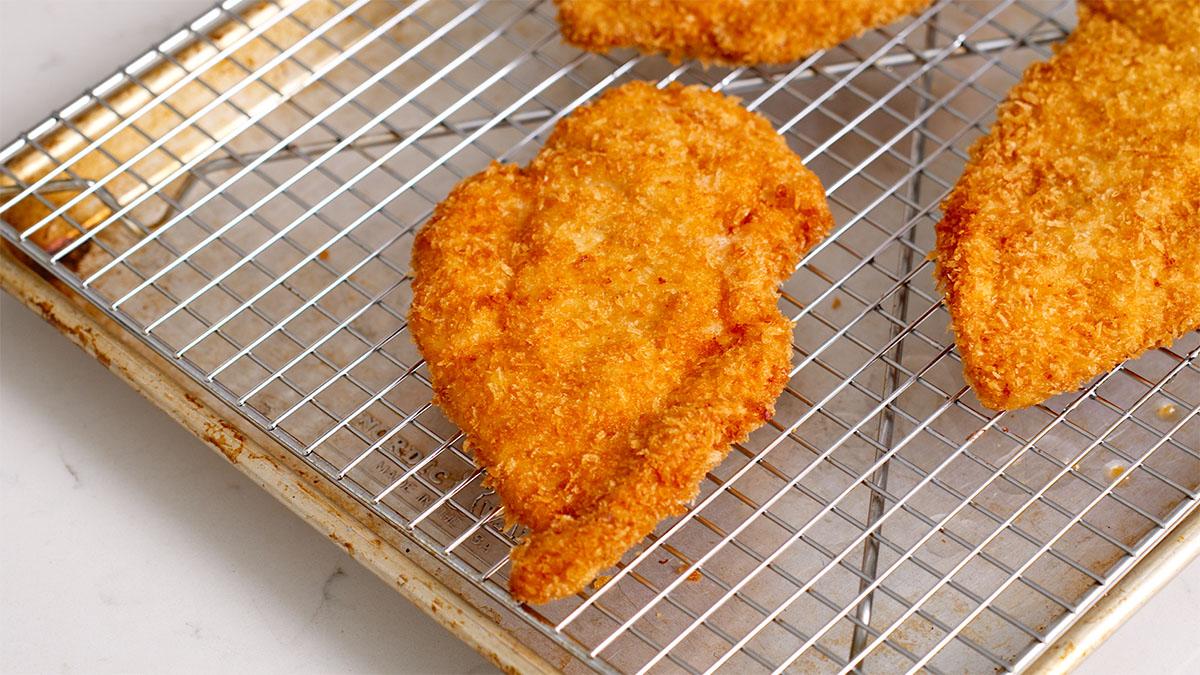 A fried chicken katsu resting on a drying rack.