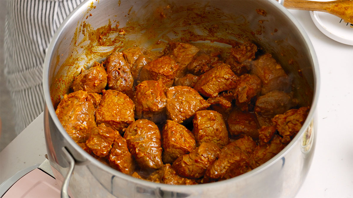 Chunks of beef and aromatics cooking in a large pot.