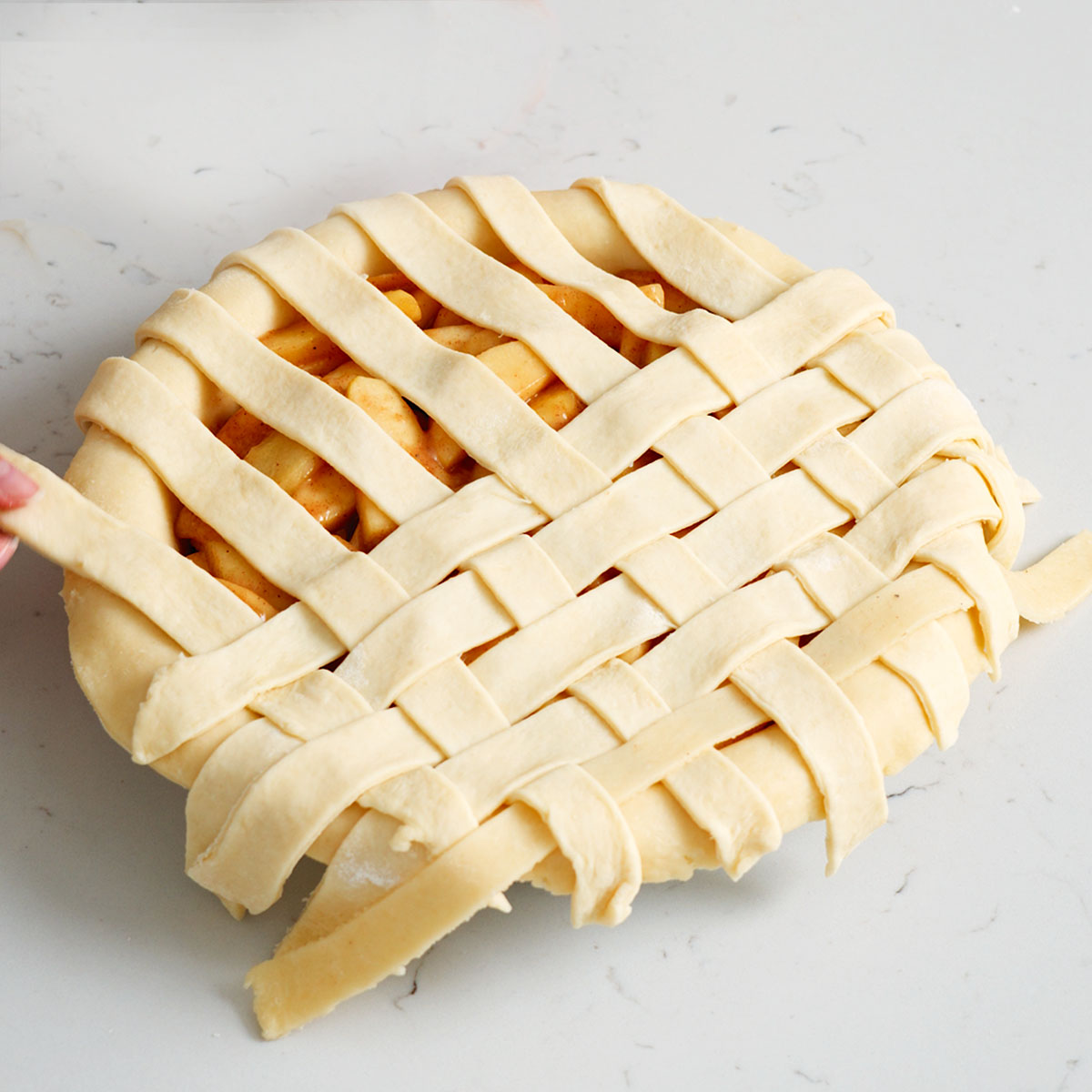 Weaving a lattice on top of an apple pie with dough strips.