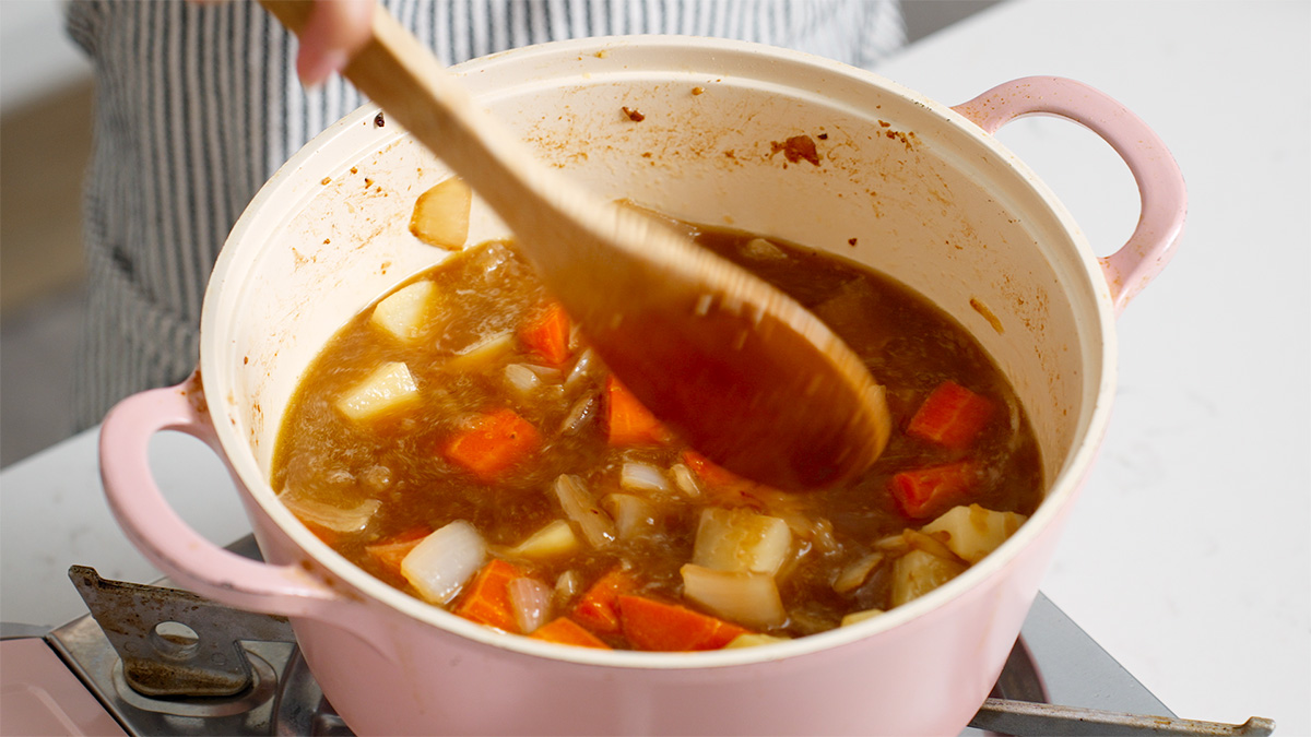 All the liquid ingredients for Japanese curry being mixed in a sauce pot with vegetables.