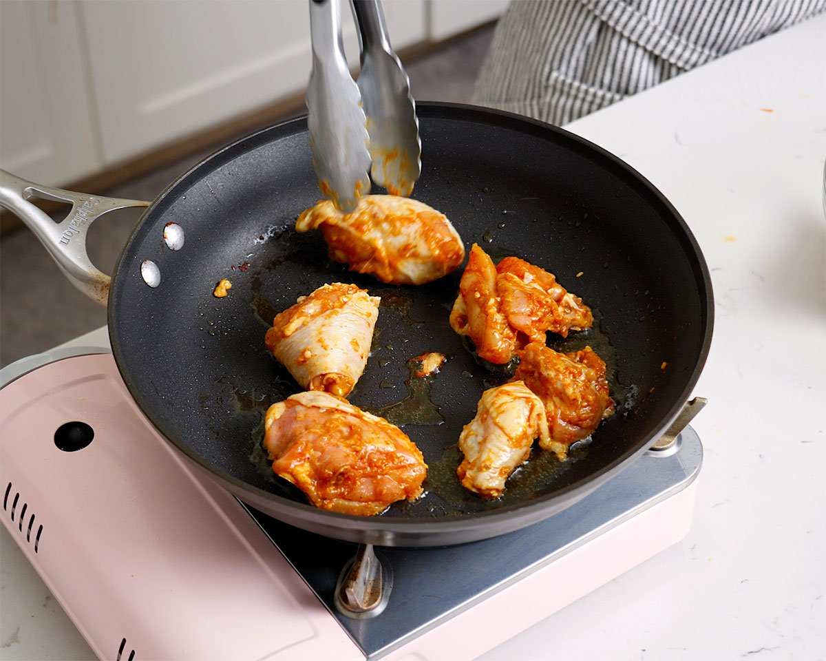 Pan frying marinaded chicken in a large skillet.