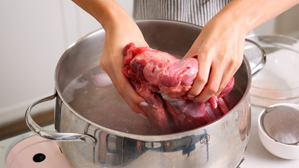 Placing beef in a large pot of boiling water to parboil.