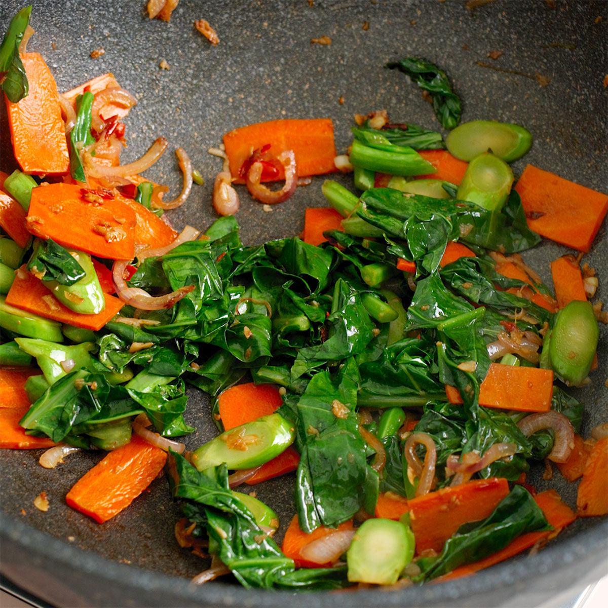 Vegetables being cooked in a large wok.