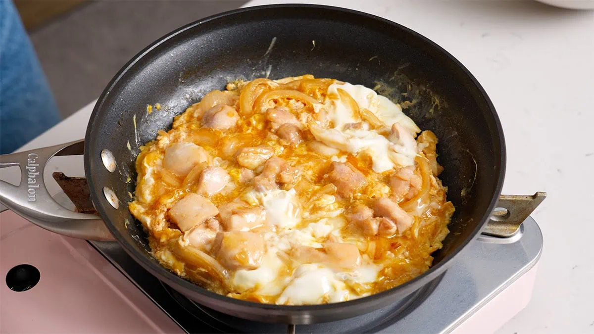Chicken, onions, and eggs being cooked in a large skillet.