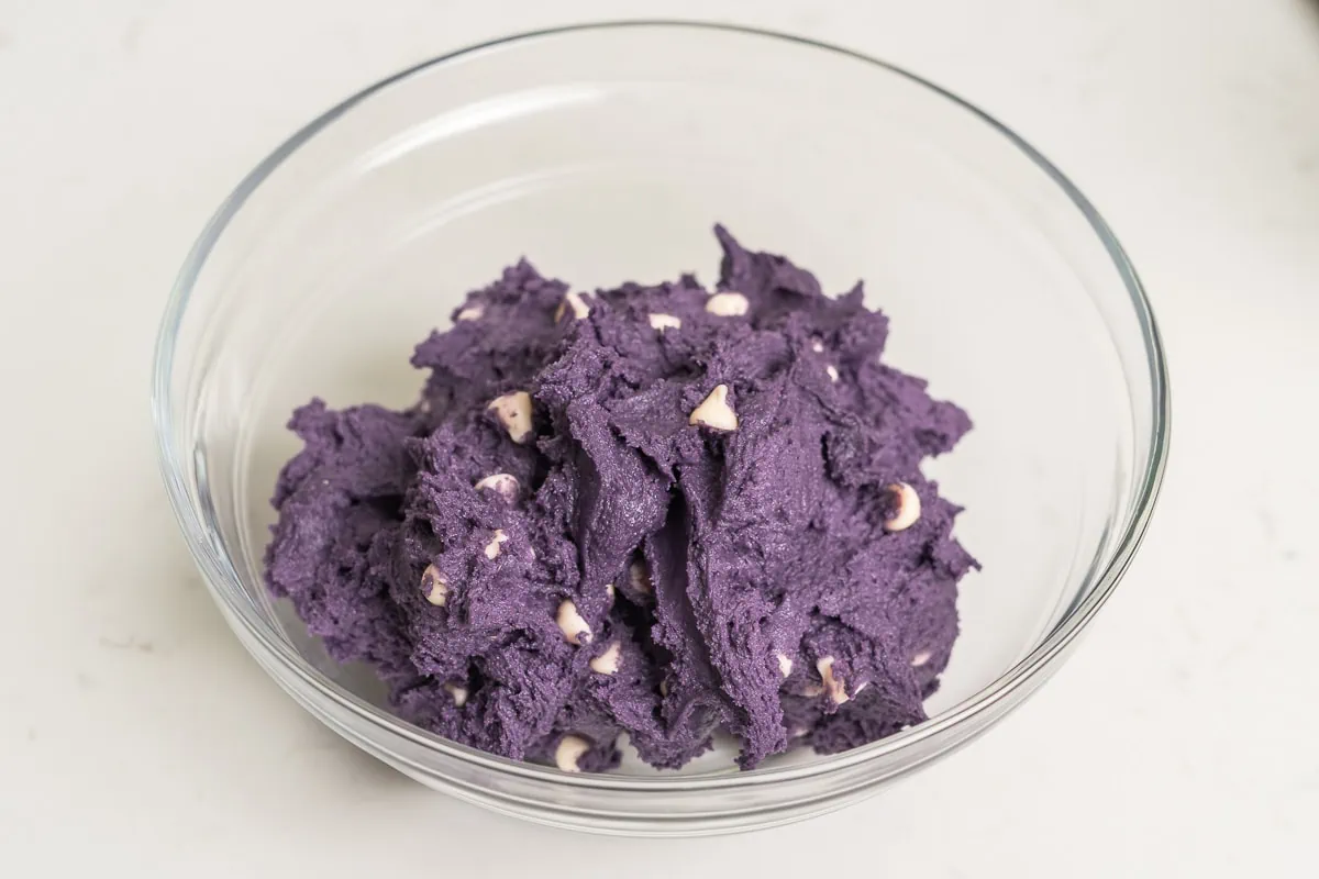 Ube cookie dough with white chocolate chips in a glass mixing bowl.