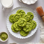 Looking down at a plate of matcha butter cookies surrounded by matcha and plates.