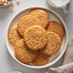 A top down view of miso peanut butter cookies piled on a plate with milk and peanuts nearby.