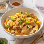 A bowl of oyakodon surrounded by table settings.